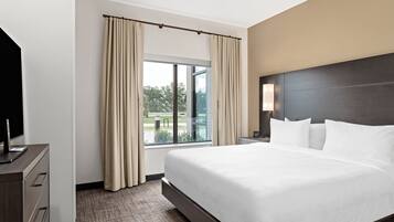 A hotel room with a large bed, a desk with a computer, a window with curtains, and a view of the outdoors.