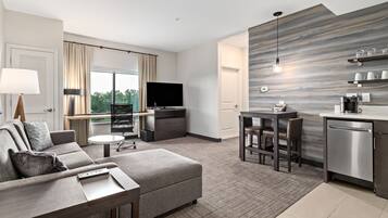 A modern hotel room with a living area, kitchenette, and a large window offering a view.