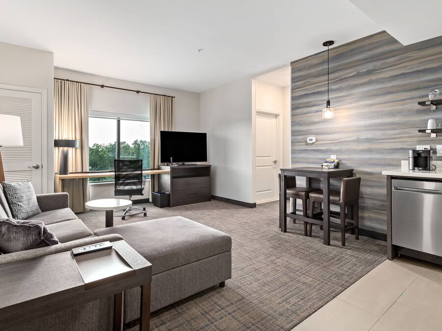 A modern hotel room with a living area, kitchenette, and a large window offering a view.