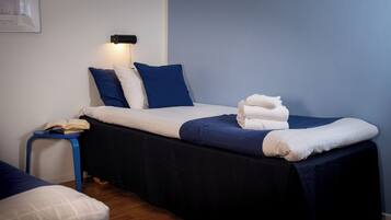 A neatly made bed with blue and white bedding, a small bedside table with a book, and a wall-mounted lamp.