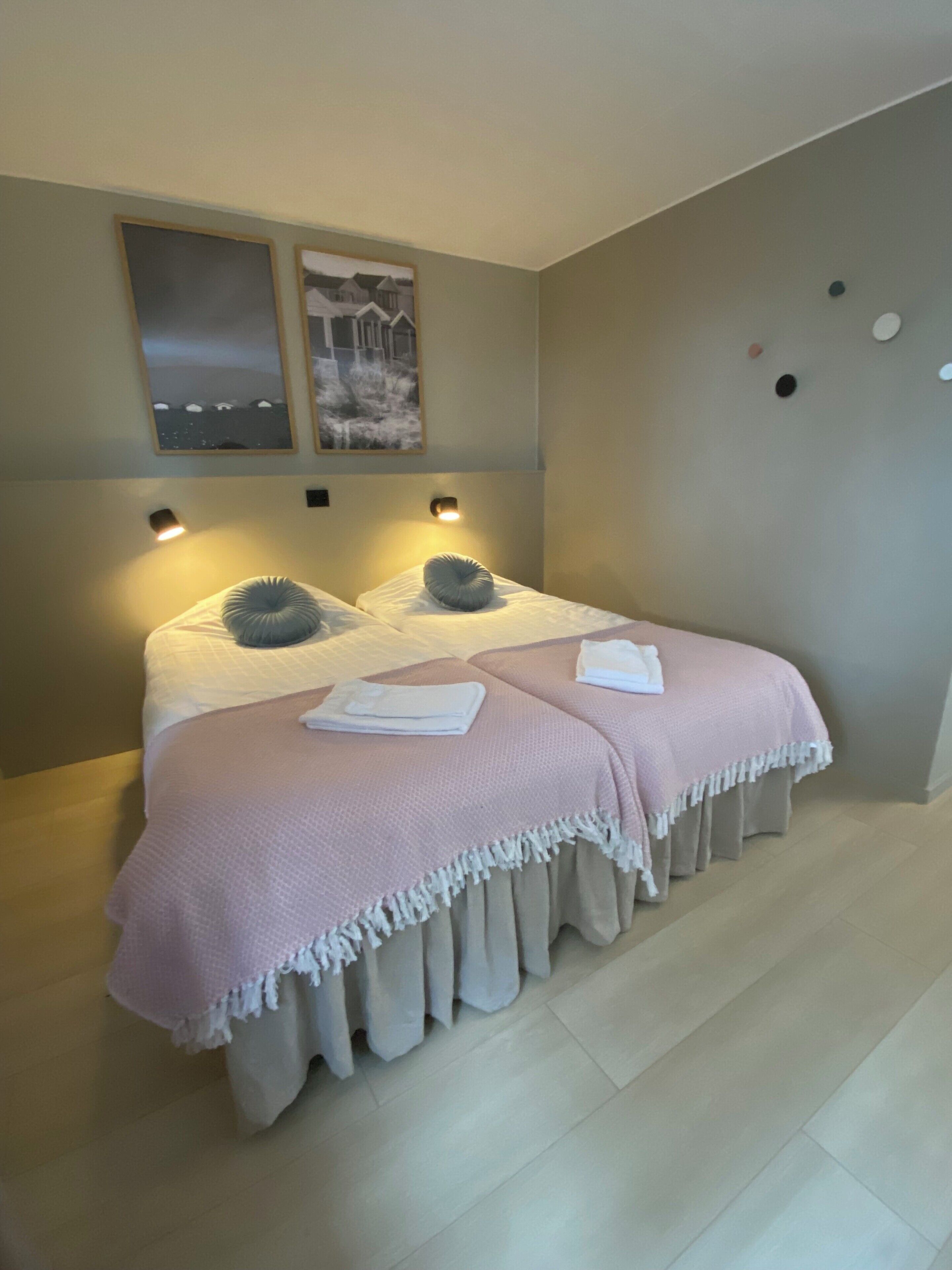 Un dormitorio con dos camas, cada una con una almohada y una manta. Hay luces fijadas en la pared sobre las camas.