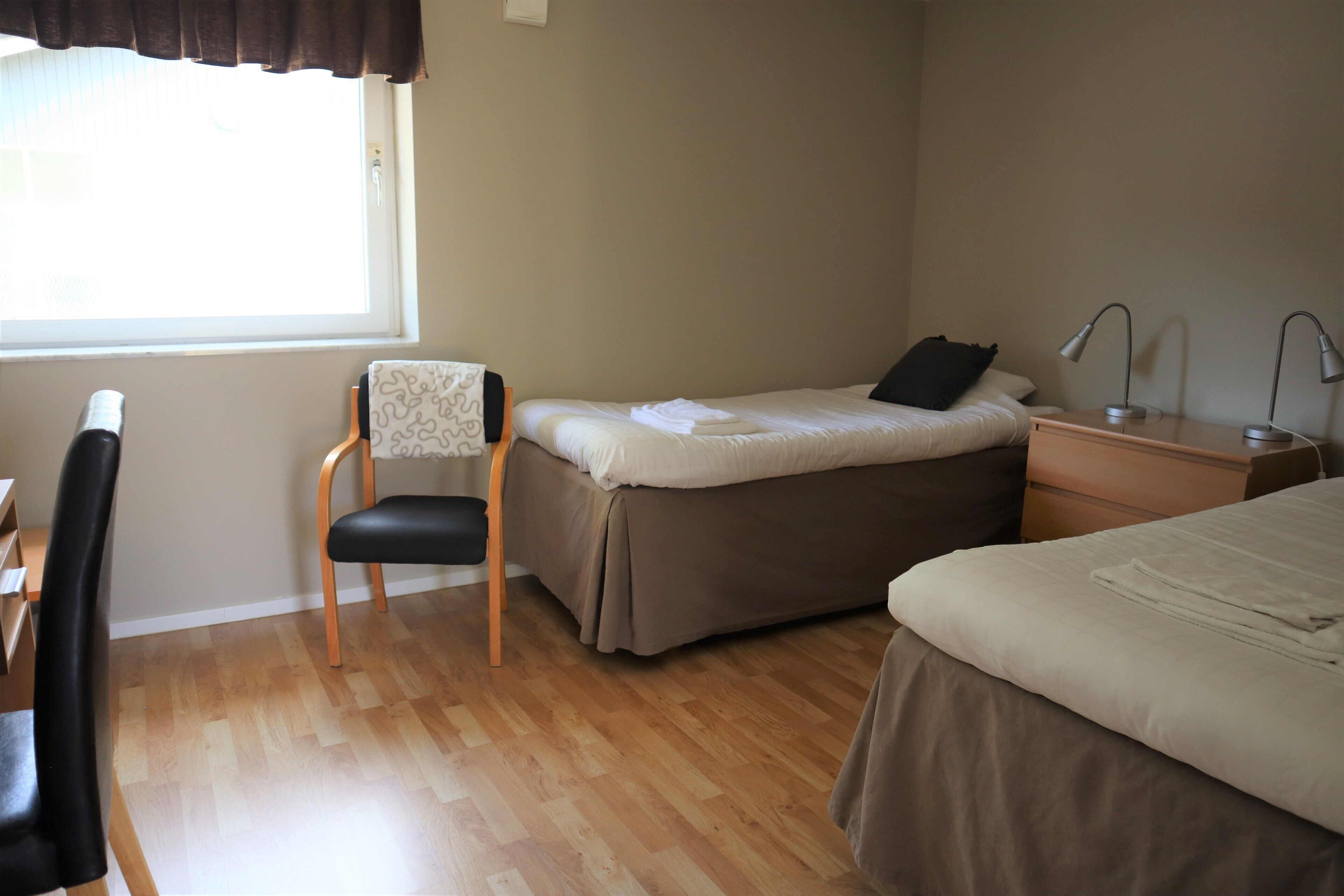 A bedroom with a bed, a chair, a desk, and a nightstand with lamps.