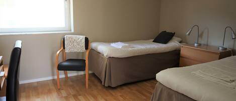 A bedroom with a bed, a chair, a desk, and a nightstand with lamps.