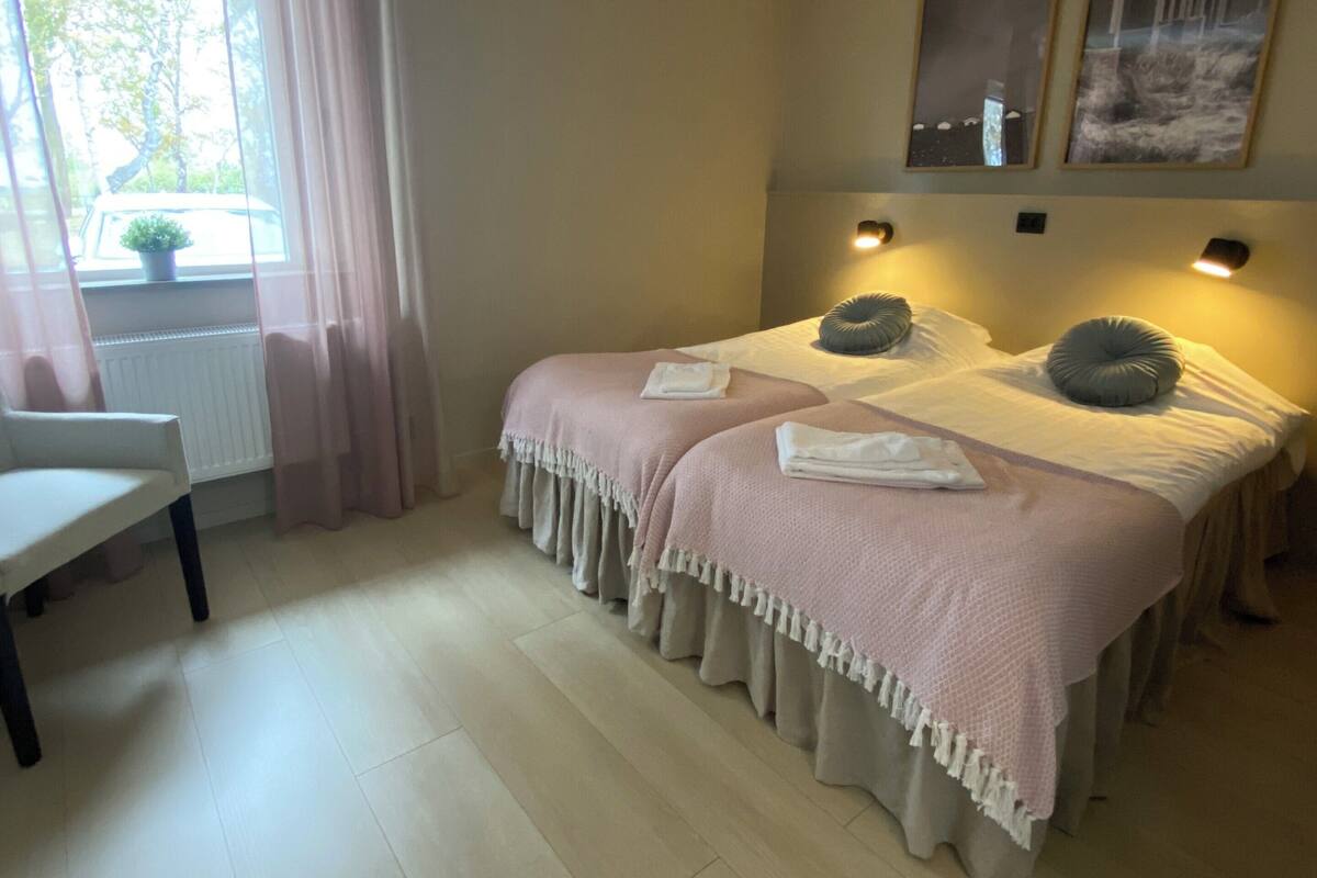 Une chambre avec deux lits, une fenêtre avec des rideaux, un radiateur et une petite table.