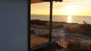 Una casa de playa con terraza de madera y vista al océano al atardecer.