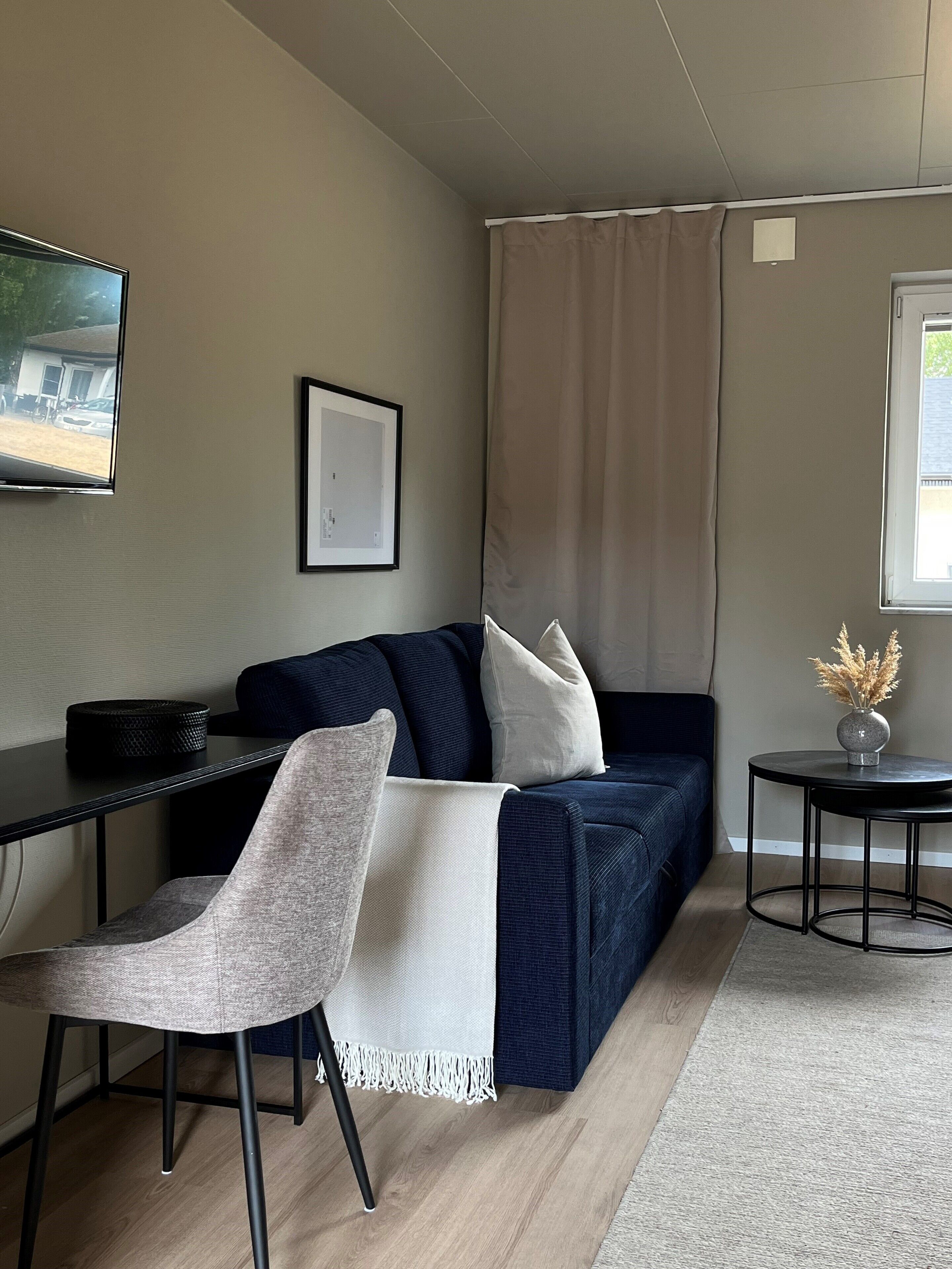 A modern living room with a dark blue sofa, a white armchair, a small round table with a vase, and a framed picture on the wall.