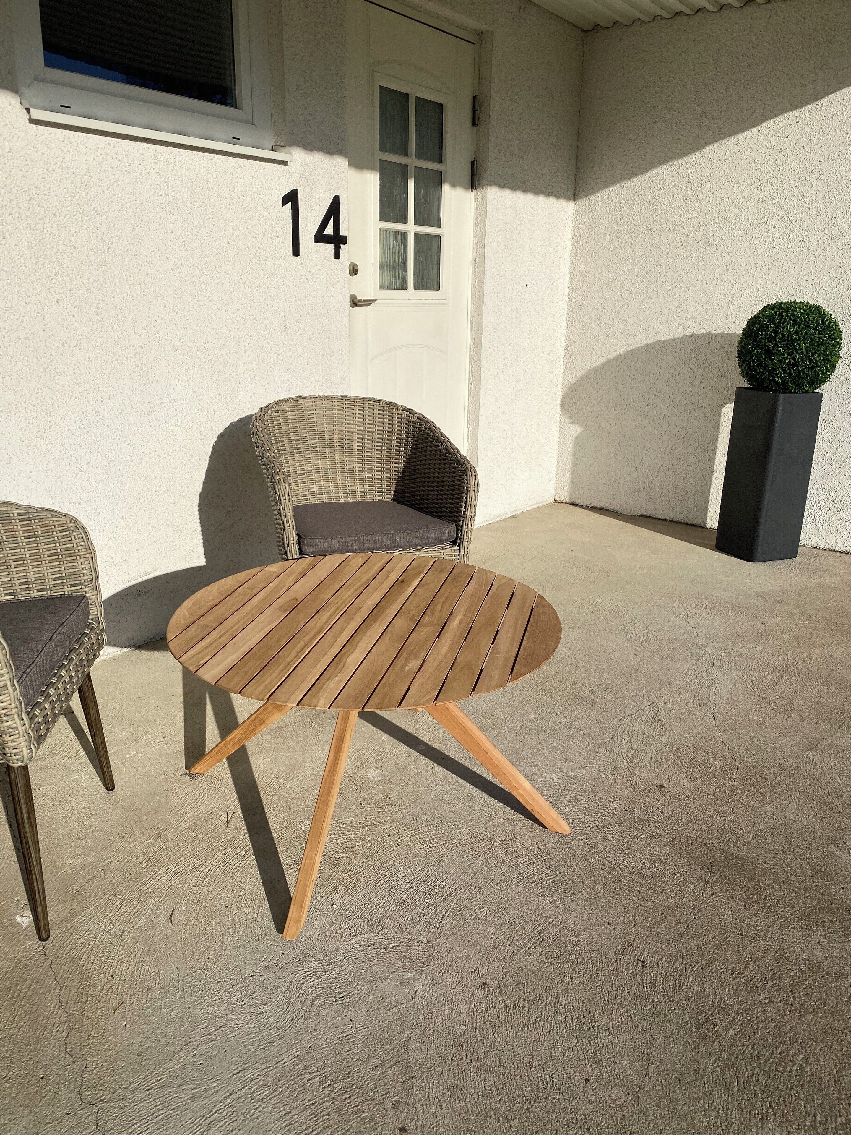 Eine Terrasse mit einem runden Holztisch und zwei Korbstühlen.