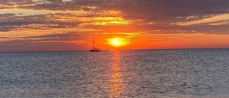 Un coucher de soleil sur une mer calme, avec un voilier à l'horizon.