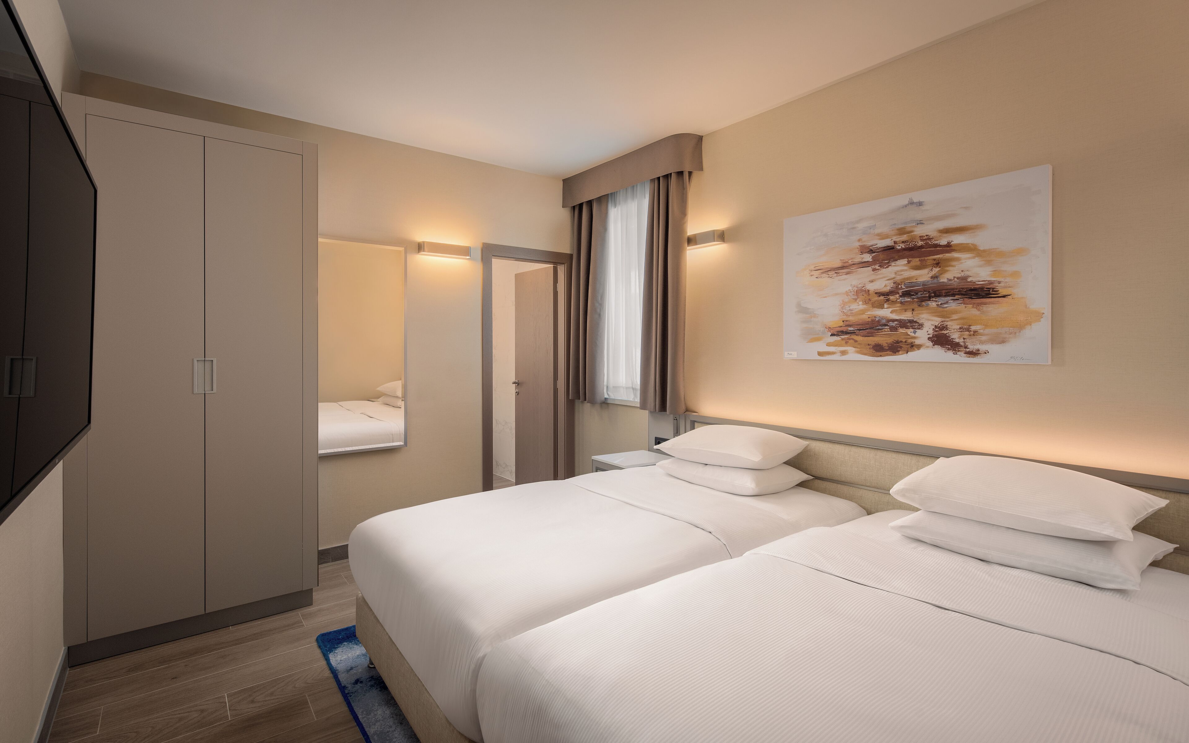 A hotel room with a bed, a wardrobe, a mirror, and a painting on the wall.