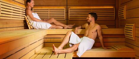 Eine Sauna mit Holzbänken, eine Person sitzt auf einer Bank, und eine weitere Person ebenfalls.