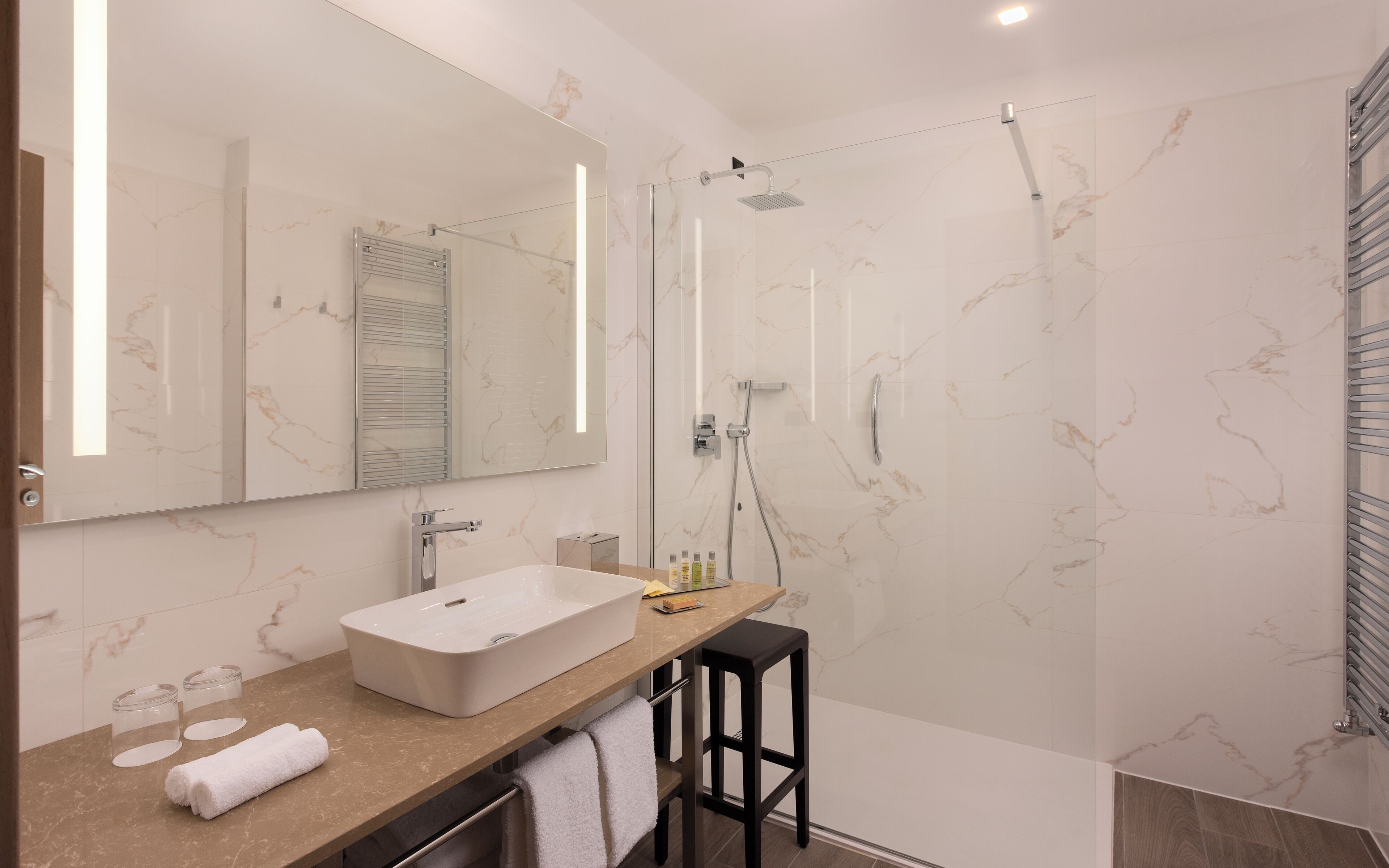 Un baño moderno con un espejo grande, un lavamanos rectangular, un cabezal de ducha manual y una ducha con paredes de vidrio.