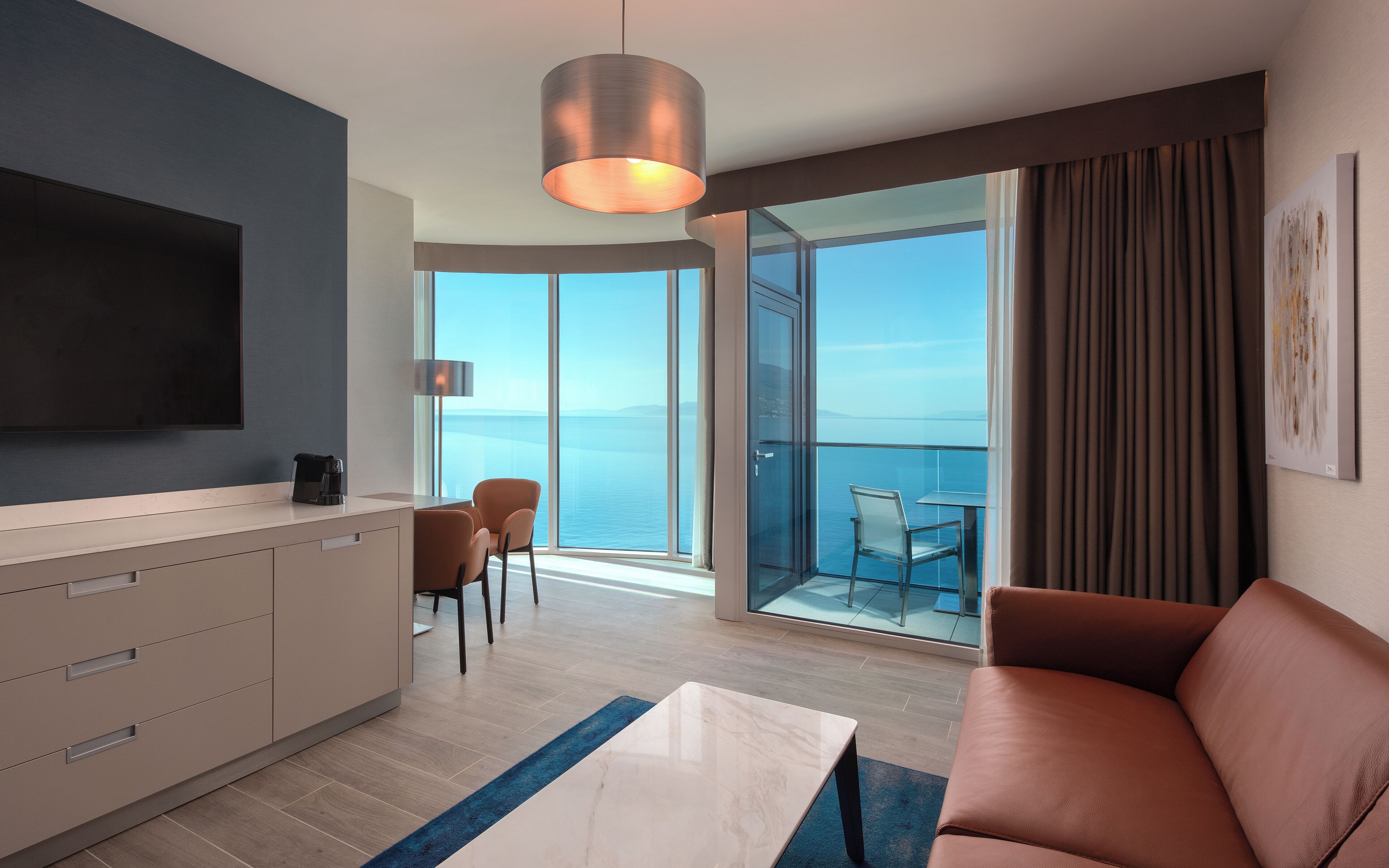 Et moderne hotelværelse med stor balkon, fladskærms-tv, sofa og spiseplads.