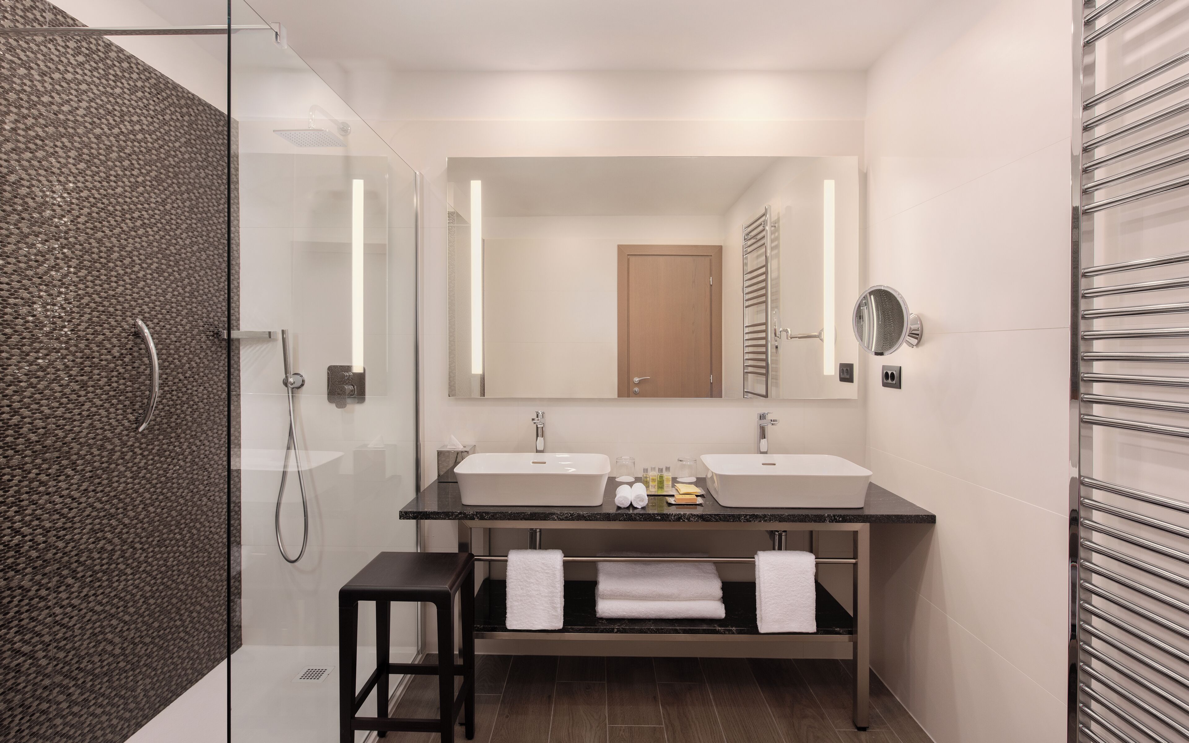 A modern bathroom with two sinks, a glass shower enclosure, a mirror, and a towel rack.