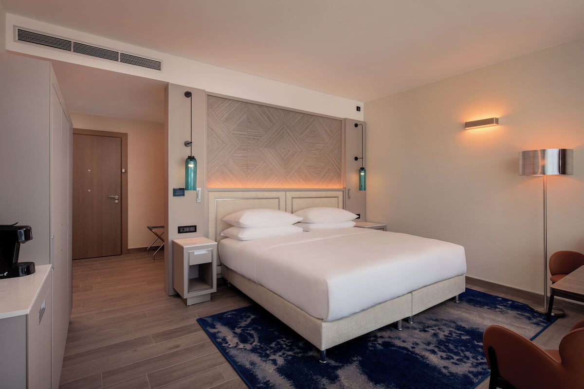 A hotel room with a bed, bedside tables, a desk, a chair, and a lamp.