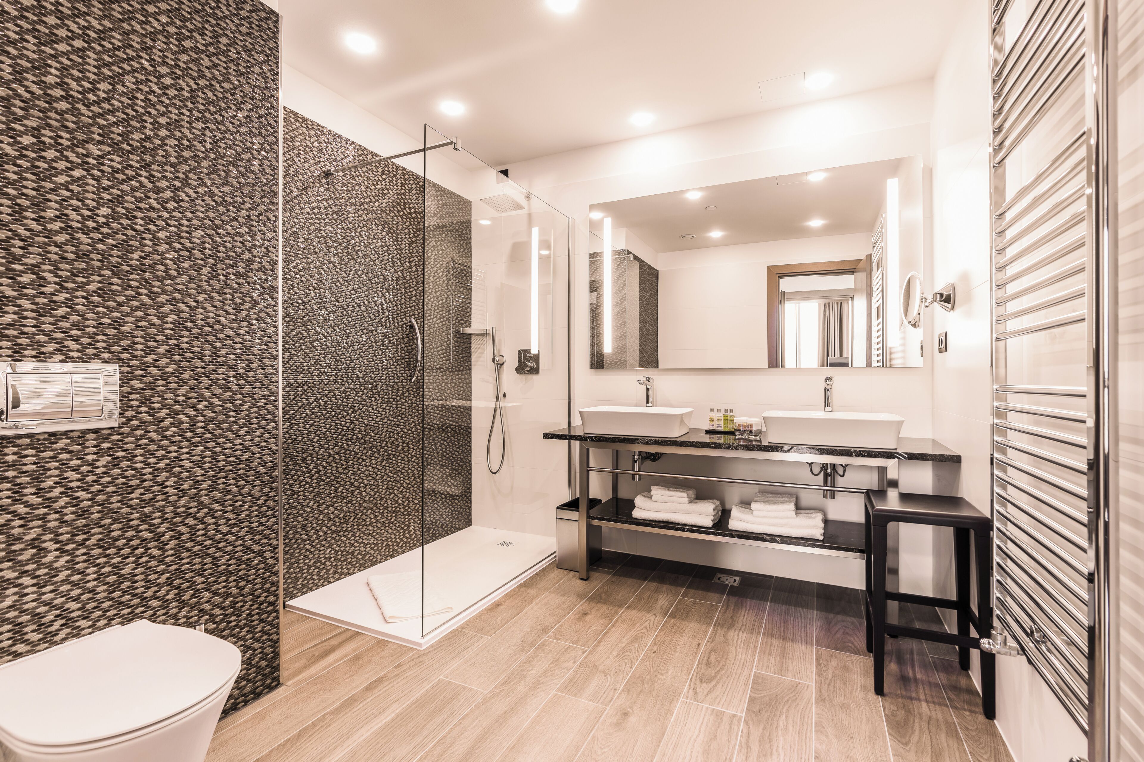 Un baño moderno con ducha separada por mampara de cristal, un lavabo e inodoro.