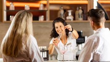 Un bar con un cantinero preparando bebidas. Se ven estantes con botellas y vasos al fondo.