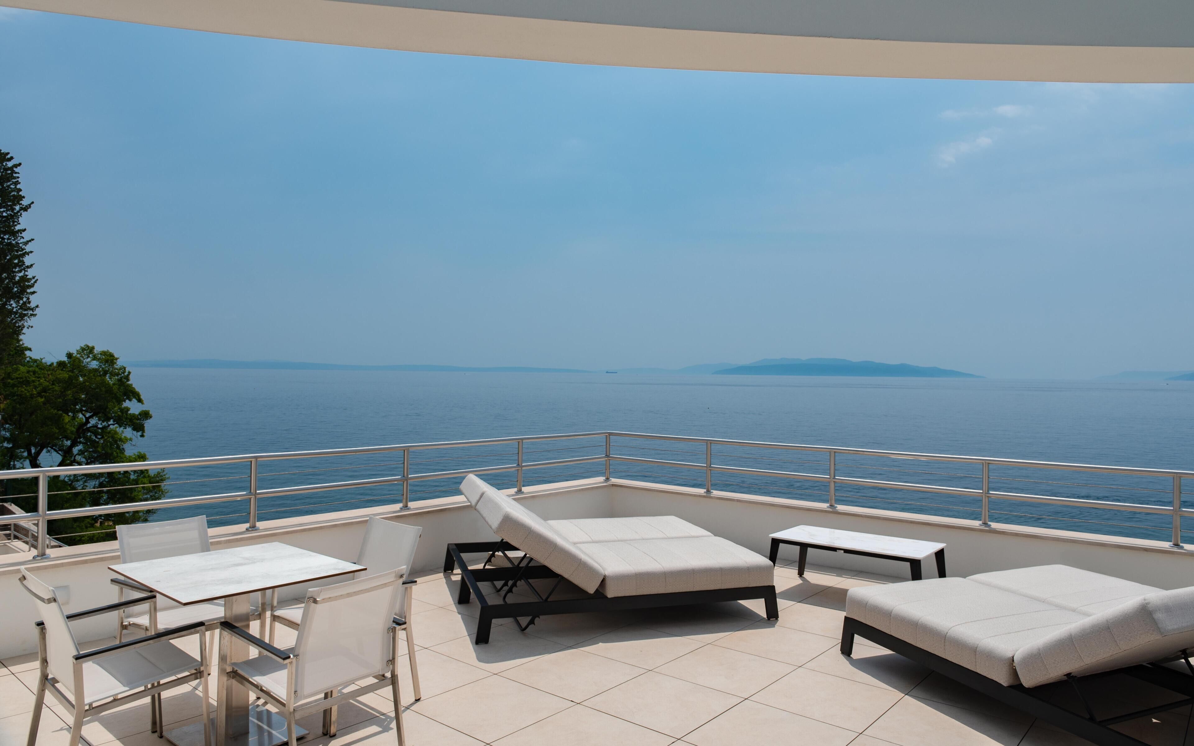 Un balcon avec vue sur la mer, une table, deux fauteuils et une petite table d’appoint.