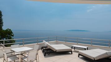 A balcony with a view of the sea, a table, two lounge chairs, and a small table.