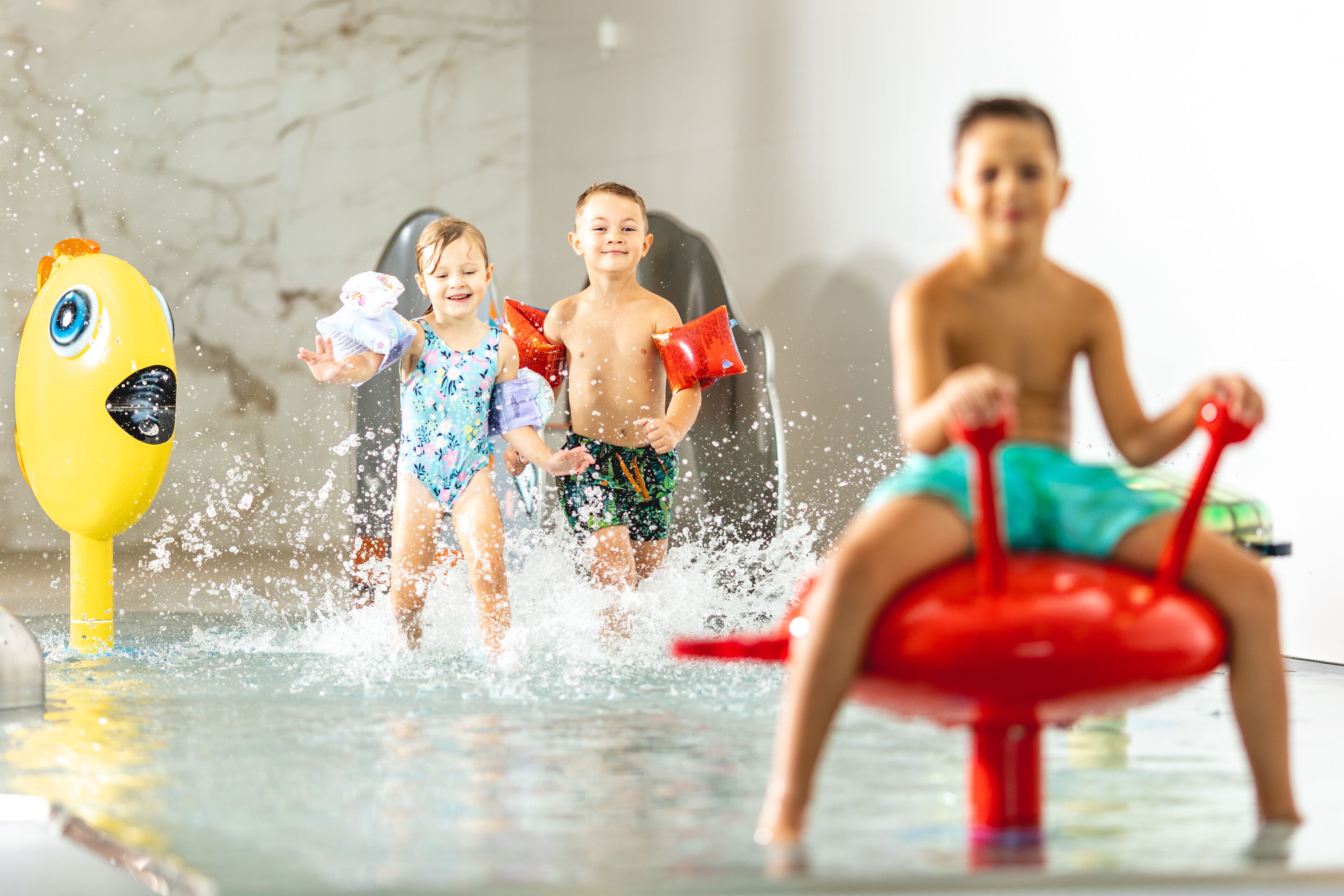 Children playing in a water feature with a yellow and red toy.
