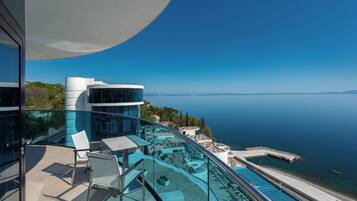 A modern building with a glass balcony overlooking a calm sea and a clear sky.