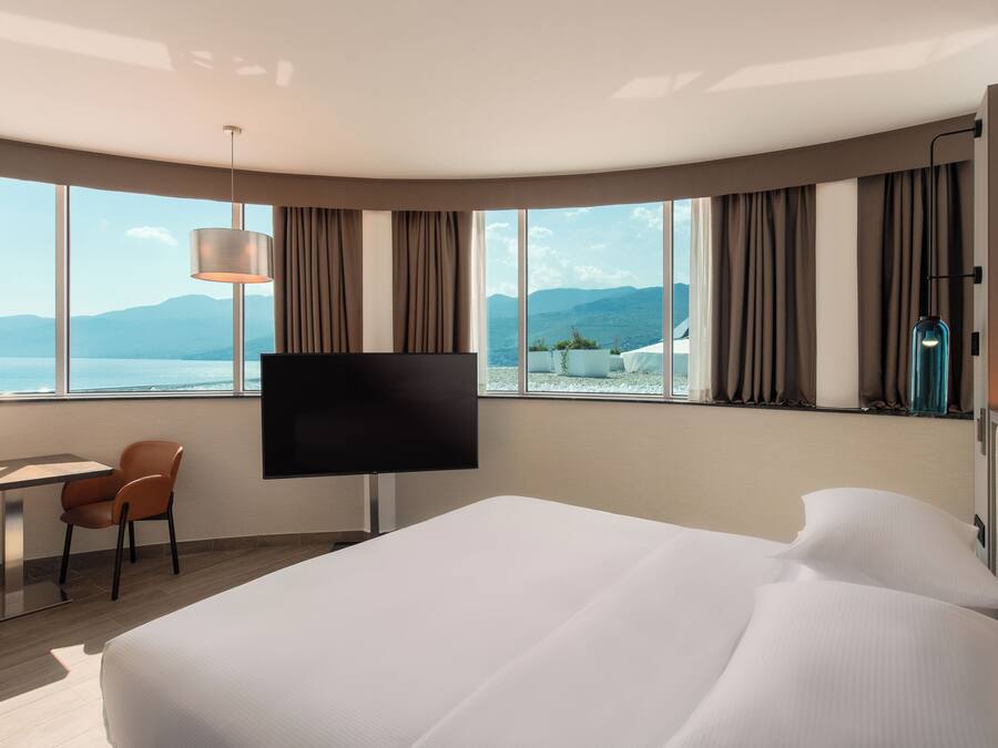 Une chambre d’hôtel avec un grand lit, une télévision, un bureau avec des chaises et une vue sur la mer.