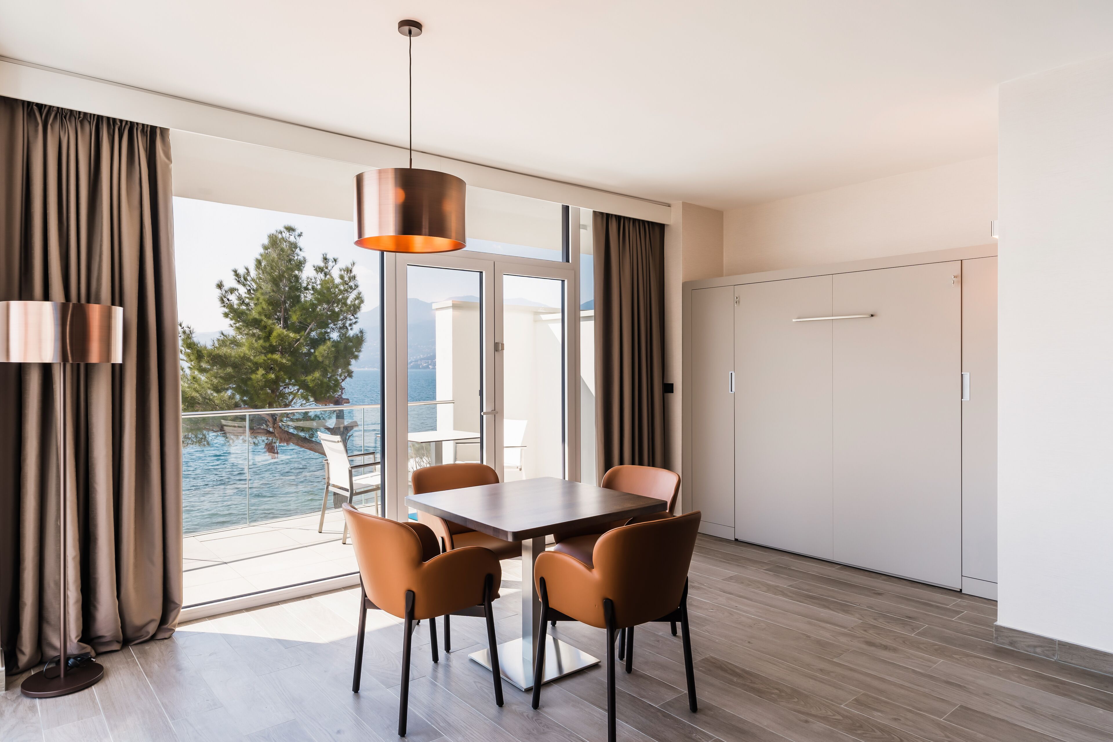 Un comedor moderno con una mesa y sillas, una lámpara colgante y vista al mar a través de grandes ventanales.