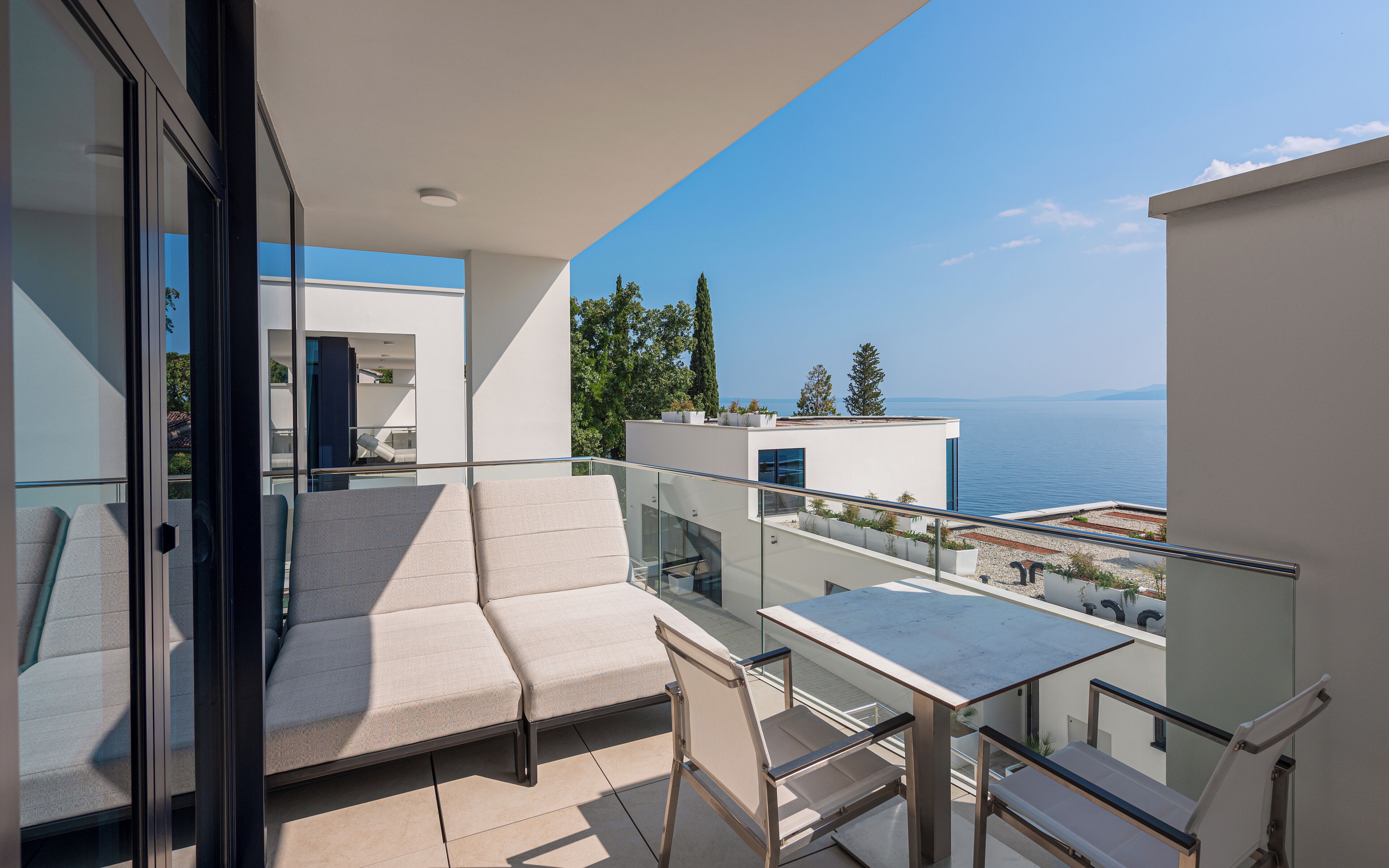 Ein Balkon mit einer Sitzecke, Tisch und Stühlen mit Blick auf ein Gewässer und Gebäude.