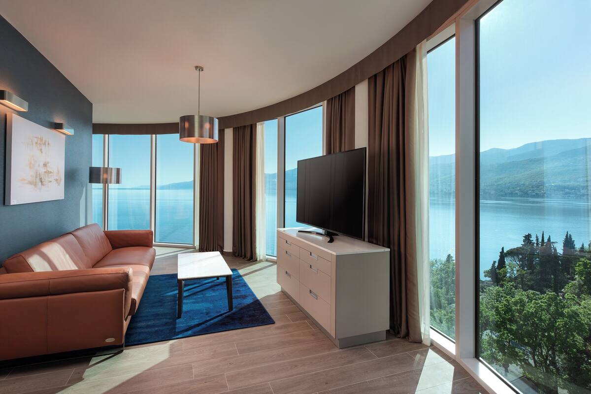 A modern living room with a sofa, TV, and large windows offering a lake view.