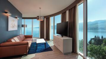 Una sala de estar moderna con sofá, televisor y ventanas amplias con vistas a un lago.