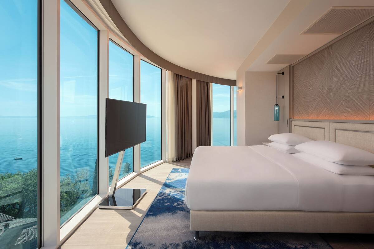 A hotel room with a large bed, a TV, and a view of the sea.