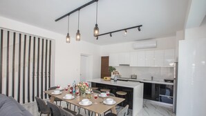 A modern kitchen with white cabinets, a dining area with a marble table, and a gray sofa. - Villa Lilia, Fabulous, New, 4BDR Protaras Villa with Pool, Close to Fig Tree Bay (Protaras)