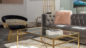 Un salon moderne avec un canapé capitonné, une table basse en verre, un fauteuil noir avec un cadre doré et un luminaire décoratif.