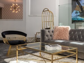 Una sala de estar moderna con un sofá capitonado, una mesa de centro de vidrio, una silla negra con estructura dorada y una lámpara decorativa.