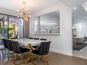 Un espace de salle à manger moderne, avec une grande table, des chaises noires aux pieds dorés et un lustre.