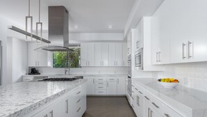 Une cuisine moderne avec des meubles blancs, un plan de travail en marbre, des appareils électroménagers en acier inoxydable et une fenêtre donnant sur un paysage verdoyant.