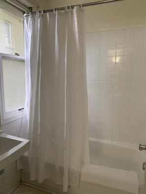 Ein Badezimmer mit einer Badewanne, einem weißen Duschvorhang und einem Fenster.