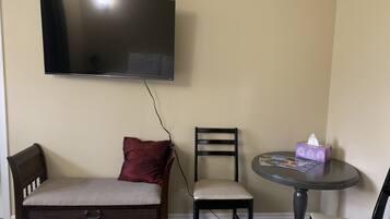 Une pièce avec un téléviseur fixé au mur, un canapé avec un coussin rouge, une chaise et une petite table ronde sur laquelle se trouve une boîte de mouchoirs.