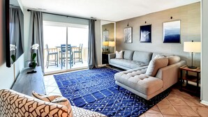 Una habitación de hotel moderna con sofá, mesa de centro, televisión y balcón con vistas.