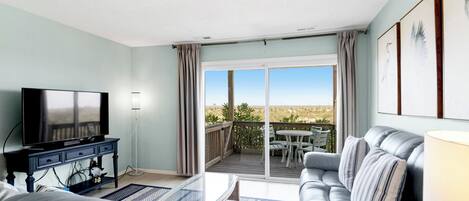 Un salón con televisor, sofá y un balcón con mesa y sillas.