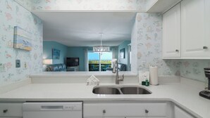 Cozinha com pia dupla, armários brancos e vista para a sala de estar.