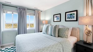 Quarto com cama grande, vista para a praia e duas molduras na parede.