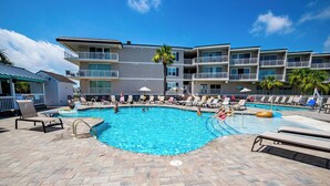 A swimming pool with lounge chairs and umbrellas, surrounded by a multi-story building with balconies. - Oceanfront Townhome w/ Pools, Pet-Friendly, Beach Access Right Out Back Door (Tybee Island)