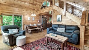 Interior de una cabaña de madera con sala de estar, comedor, cocina y habitación en un entrepiso.
