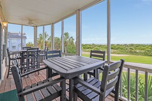 Un patio techado al aire libre con una mesa y sillas, con vistas a un paisaje cubierto de césped y una masa de agua.