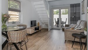 En moderne stue med en sofa, et spisebord med stole, et fjernsyn og en trappe til et udendørs område.