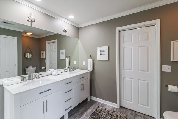 A bathroom with a double vanity, a large mirror, a toilet, and a door with a picture frame.