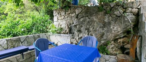 An outdoor patio with stone walls, a table covered with a blue tablecloth, and two chairs.