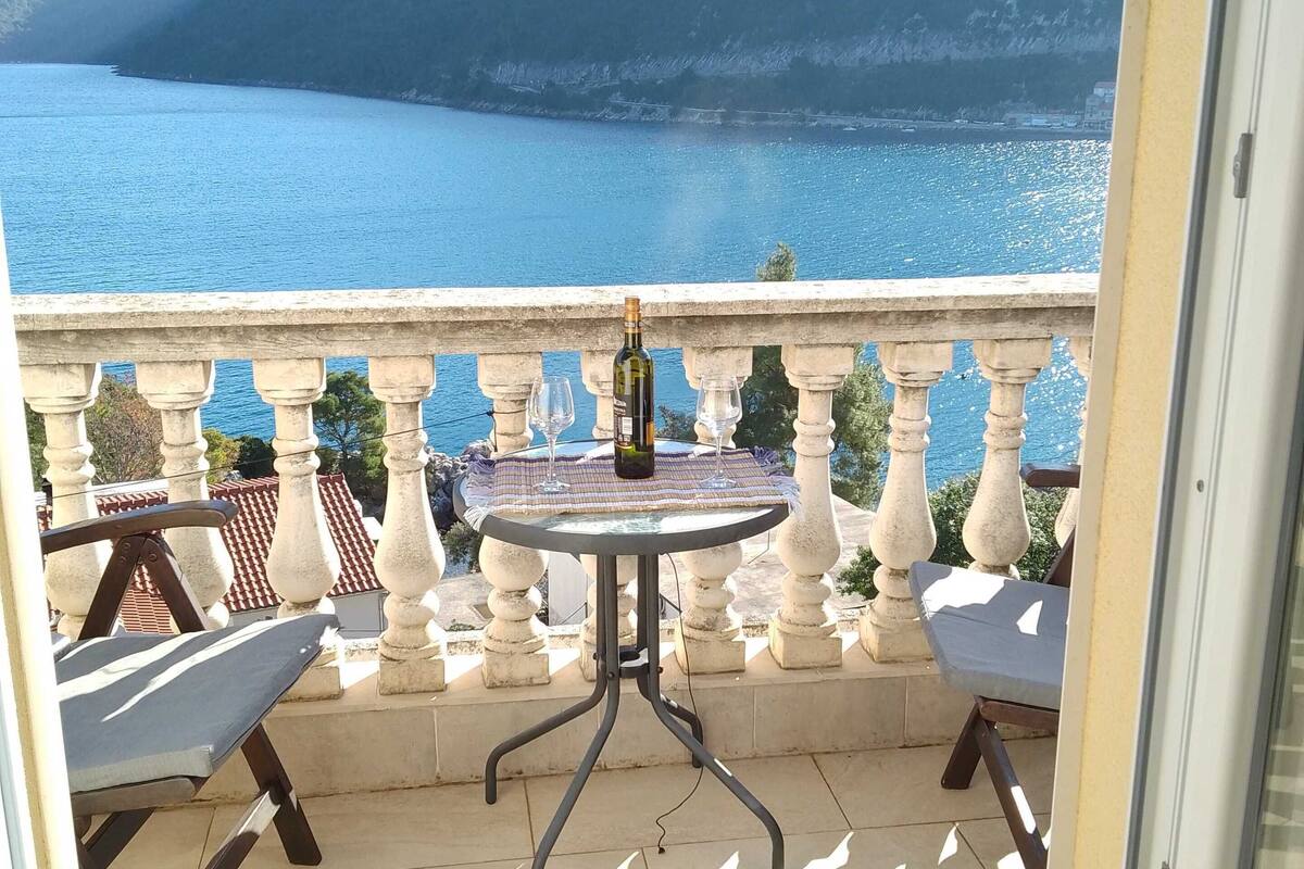 A balcony with a table and chairs, overlooking a body of water and a mountain.
