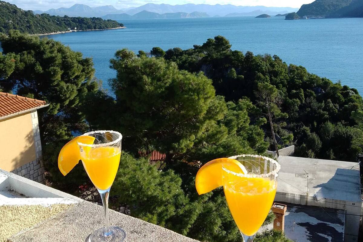 Two cocktails on a balcony overlooking a scenic lake with mountains in the background.