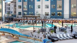 A pool area with lounge chairs, a slide, and a building with multiple windows. - Zions Gateway Escape (Hurricane)